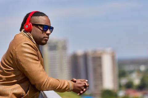 Black man stands on observation deck leaning over fence listening to music Stock Photos