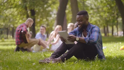 Black man with tablet sitting on grass Stock Footage 114837869