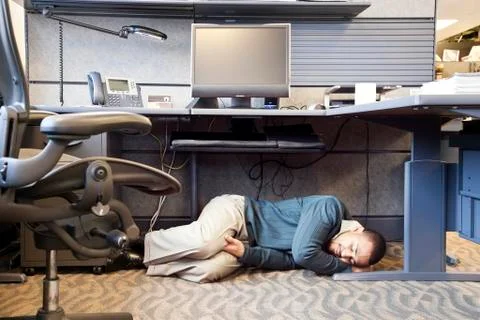 A Black man taking a nap under his desk in a corporate office Stock Photos