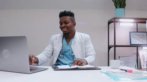 Black man talking in video chat on laptop, wearing medical gown and stethoscope Vídeo Stock 166664642