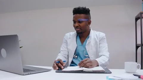 Black man talking in video chat on laptop, wearing medical gown and stethoscope Vídeo Stock 166665156