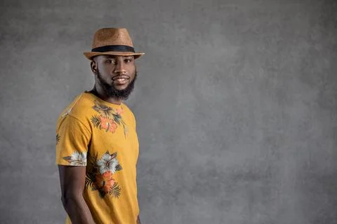 Black man touching hat while standing sideways against gray background Stock Photos