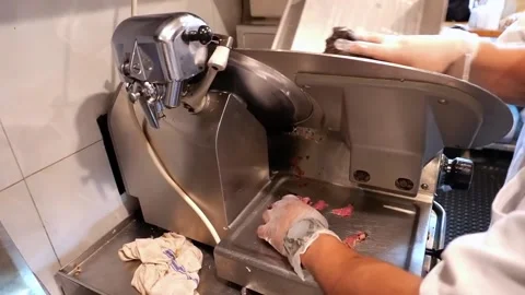 Black man uses a machine to slice thin pieces of beef to make sandwiches Stock Footage 172050248