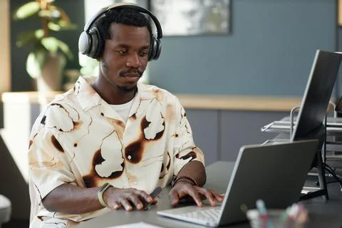 Black Man Using Computer and Tech Gadgets in Headphones at Modern Workplace Stock Photos