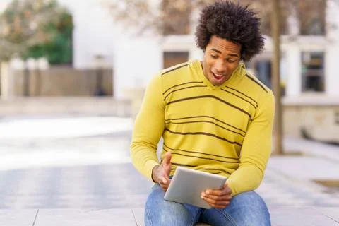 Black man using a digital tablet sitting on a bench outdoors. Foto stock