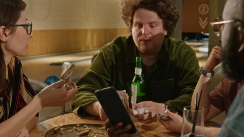 Black Man Using Mobile Payment App while Splitting Bill with Friends at Bowling Stock Footage 337101337