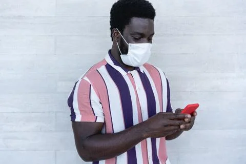 Black man using mobile phone - African guy wearing face protective mask while Stock Photos