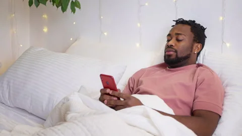 Black man using smartphone after waking up, internet addiction problem of modern Stock Footage 262695232