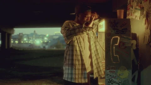 Black Man Using Warmly Lit Payphone under Dark Urban Overpass Video stock 285667787