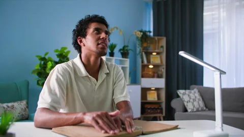 Black man with vision problems reads a braille book while sitting at a table in Stock Footage 254702903
