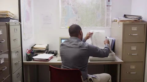 Black man waits for document to finish printing in small cluttered office Stock Footage 133356091