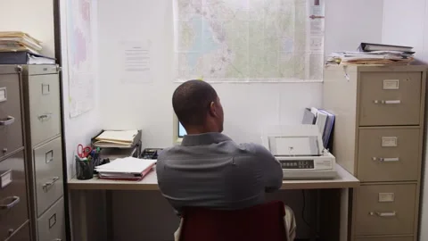 Black man waits for printer to start printing in small cluttered office Stock Footage 133355968