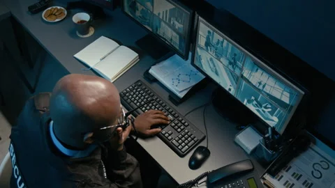 Black Man Watching Screens with Cctv Feed and Using Portable Radio at Night Stock Footage 330609785