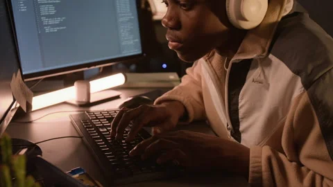Black Man Wearing Headphones Programming Software on Computer at Night Stock Footage 336717113