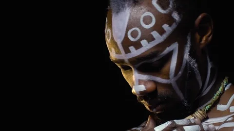 A black man in white patterns with a necklace on his neck turns and looks into Stock Footage 82224964