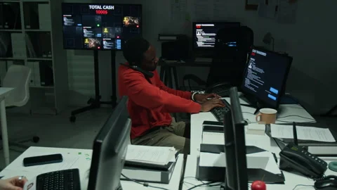 Black Man Working on Computer and Talking on Phone in Scam Call Center Stock Footage 346703918