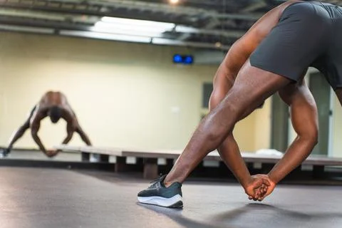 Black man working on his flexibility in front of gym mirror Stock Photos