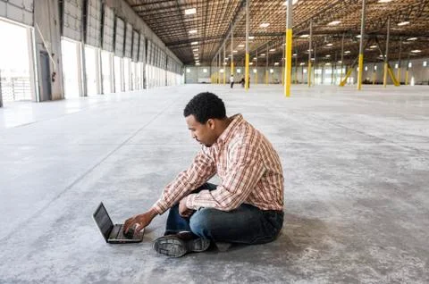 Black man working on lap top computer in front of loading dock doors in a new Stock Photos