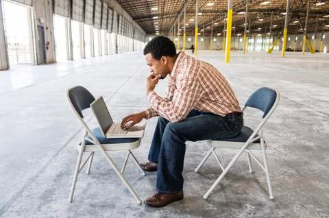 Black man working on lap top computer in front of loading dock doors in a new Foto stock