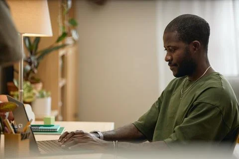 Black Man Working on Laptop Computer at Home Office Desk 写真素材