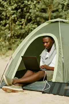 Black Man Working on Laptop Inside Tent While Camping Outdoors Stock Photos