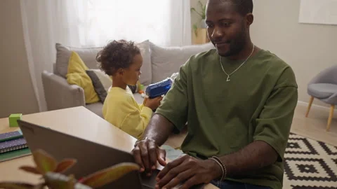 Black Man Working Remotely on Laptop with Son Playing at Home Stock Footage 345490824