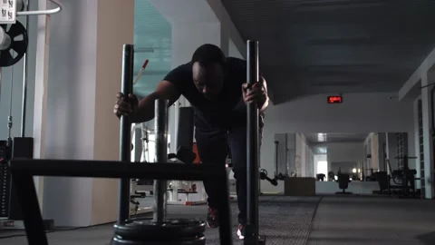 Black man workout pushes a heavy weight trolley in the gym in slow motion Stock Footage 225715305