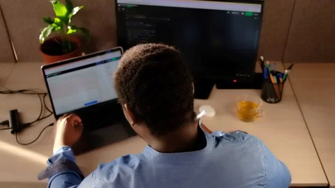 Black Man Writing Lines of Code On Desktop PC With Two Monitors and a Laptop Stock Footage 240830295