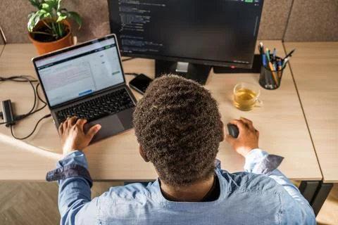Black Man Writing Lines of Code On Desktop PC With Two Monitors and a Laptop 스톡 사진