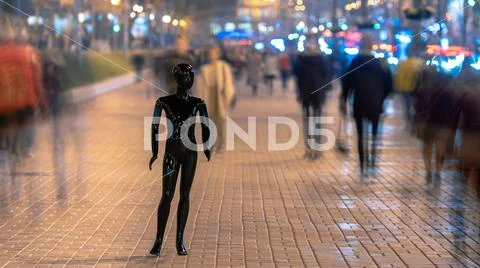 The black mannequin standing on the evening street with people Stock Photos