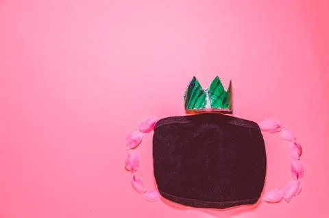 Black mask with green crown on a pink background Stock Photos
