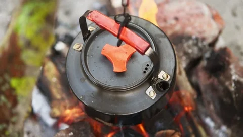 Black metal kettle with orange handle heating on open bonfire outdoors in n.. Vidéo 344338785