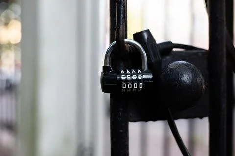 Black metal lock with a letter code hangs from a closed black metal door 写真素材
