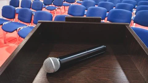 Black microphone with  silver mesh grille is mounted on dark wood lectern. Ro Stock Photos