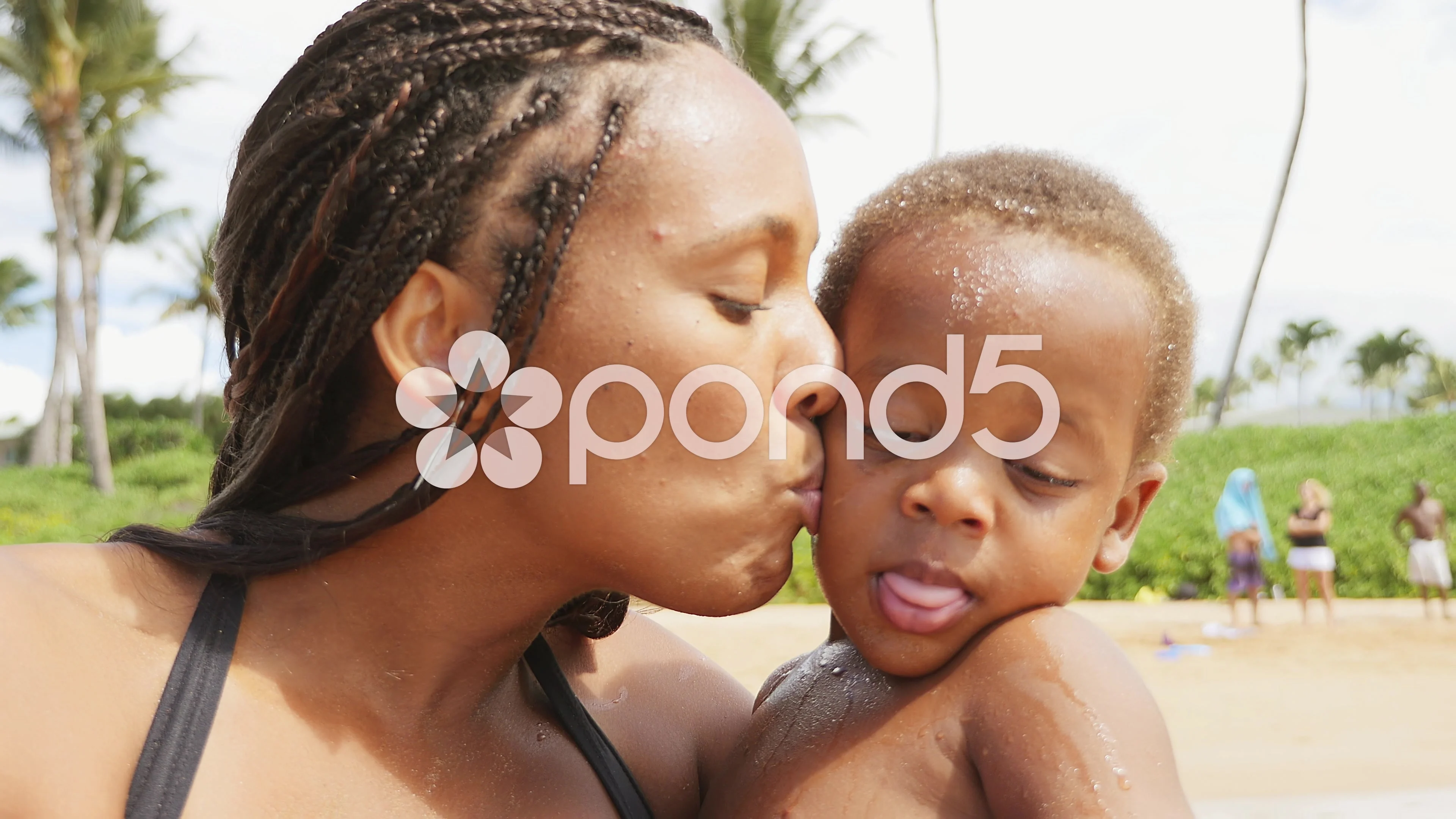 Black mother and toddler blowing kisses on a beach