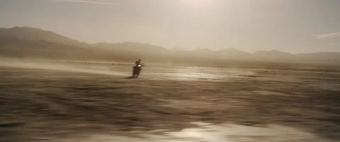 Black motorcycle approaches while camera moves across lake bed Stock Footage 136495020