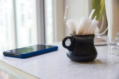 A black mug with a toothpicks in a package in it sits on a table next to a cell Stock Photos