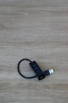 Black multi-port USB hub with coiled cable on wooden desk, minimalist layout. Stock Photos