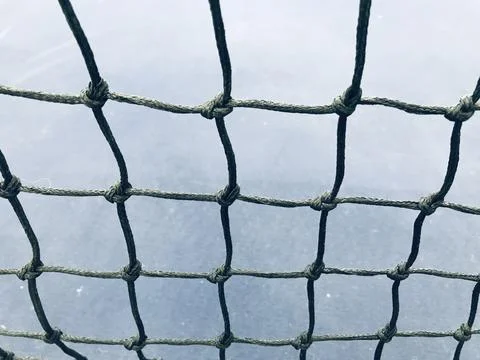 Black net stretched into a grid with a blurred blue tennis court on background Photos