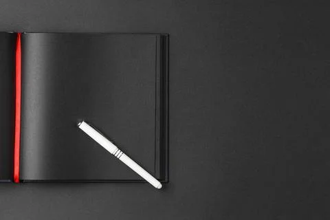 Black notebook on dark background with a white pen Stock Photos