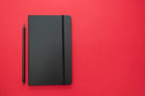Black notebook on red background. Top view of working table, work space. abst Foto stock