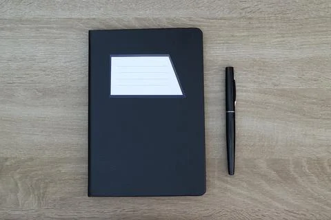 Black notebook with white label and pen on wooden desk Stock Photos