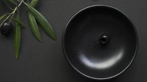Black olives filling empty black bowl on black background Stock Footage 334695210