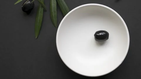 Black olives placed with tweezers into empty white bowl on black background.. Stock Footage 334637220