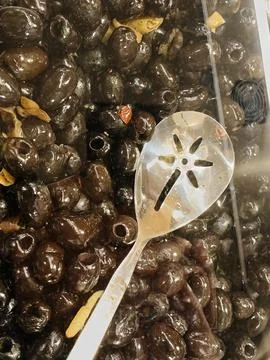Black olives in plastic container with spoon Stock Photos
