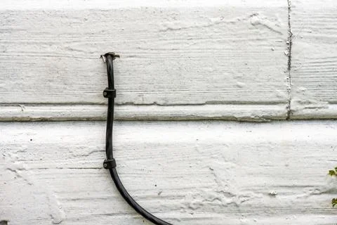 Black optical fibre data cable going into a white wooden wall of a house. Stock Photos