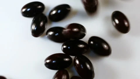 Black oval spindle-shaped capsules in a shiny gel shell pour down. Real time, na Stock Footage 144854926