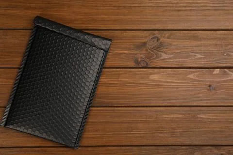 Black padded envelope with bubble wrap on wooden background, top view. Space  Stock Photos