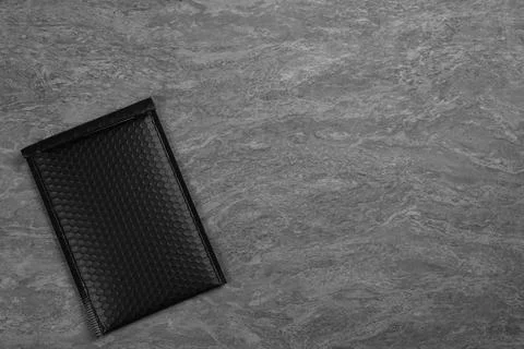 Black padded envelope with bubble wrap on grey background, top view. Space fo Stock Photos