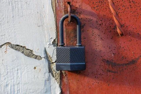 Black padlock secures rusted red and white door Stock Photos